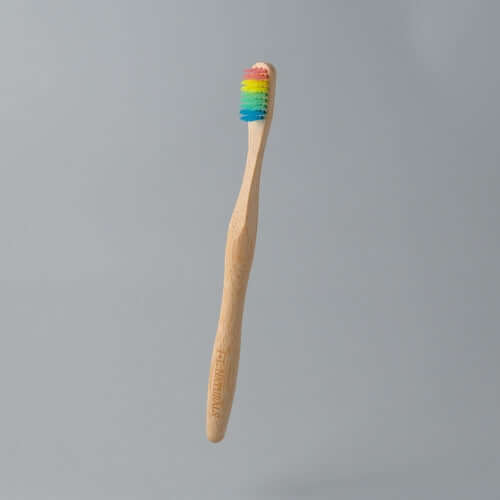 Eco-friendly bamboo toothbrush with rainbow-colored bristles floating against a grey background.