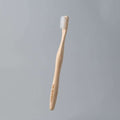 Eco-friendly bamboo toothbrush with white bristles on a plain grey background