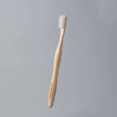 Eco-friendly bamboo toothbrush with white bristles on a plain grey background
