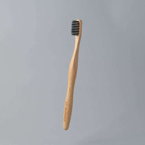 Eco-friendly bamboo toothbrush with black bristles against a plain gray background