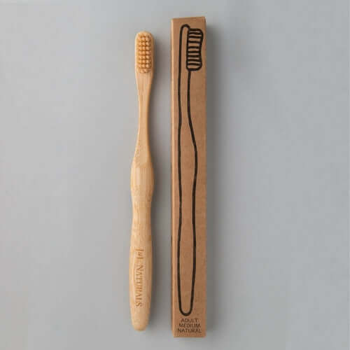 Eco-friendly bamboo toothbrush with medium bristles and its cardboard packaging.