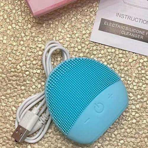 Light blue electric silicone facial cleanser with USB charging cable on a textured surface