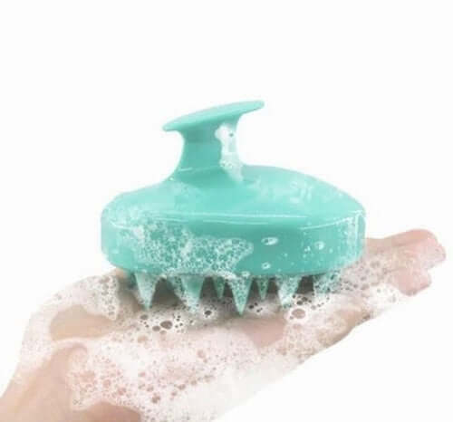 Light blue silicone scalp massager brush with soap foam on a hand