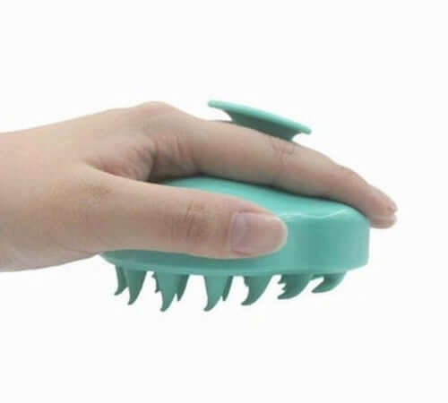 Hand holding a turquoise silicone scalp massager and shampoo brush